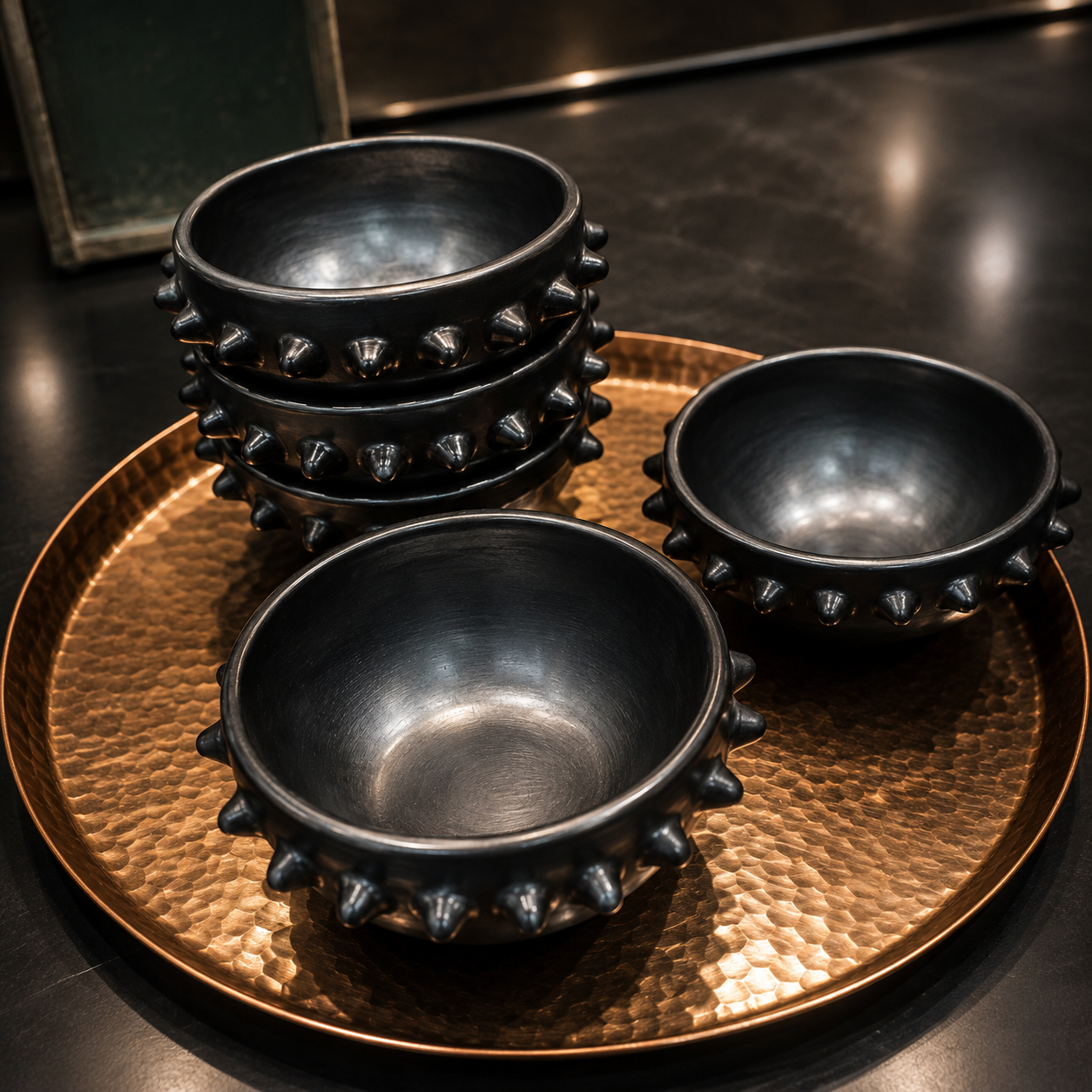 Bowls de cerámica negra con picos sobre charola circular de cobre martillado