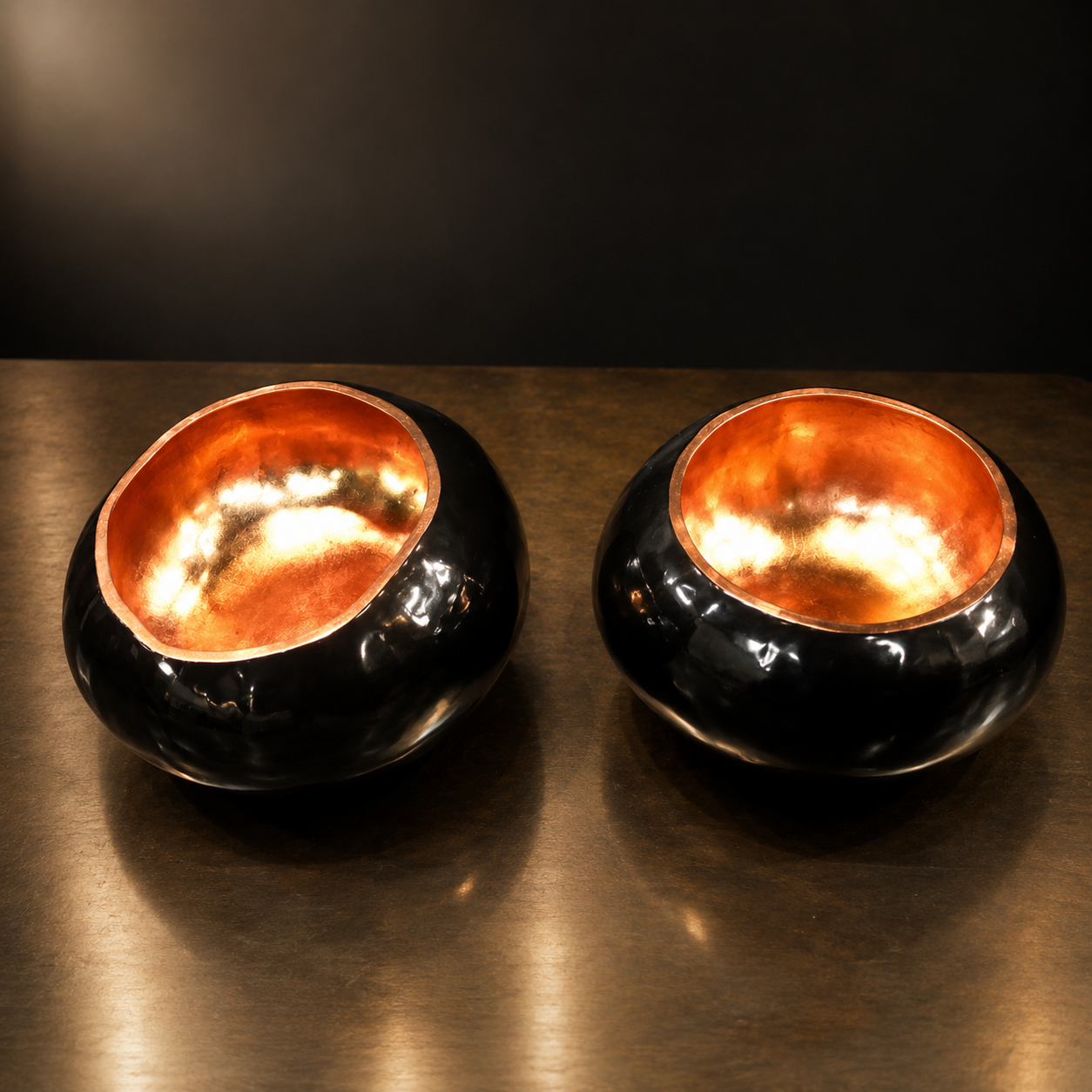 Par de cuencos negros con interior de cobre martillado sobre mesa de latón