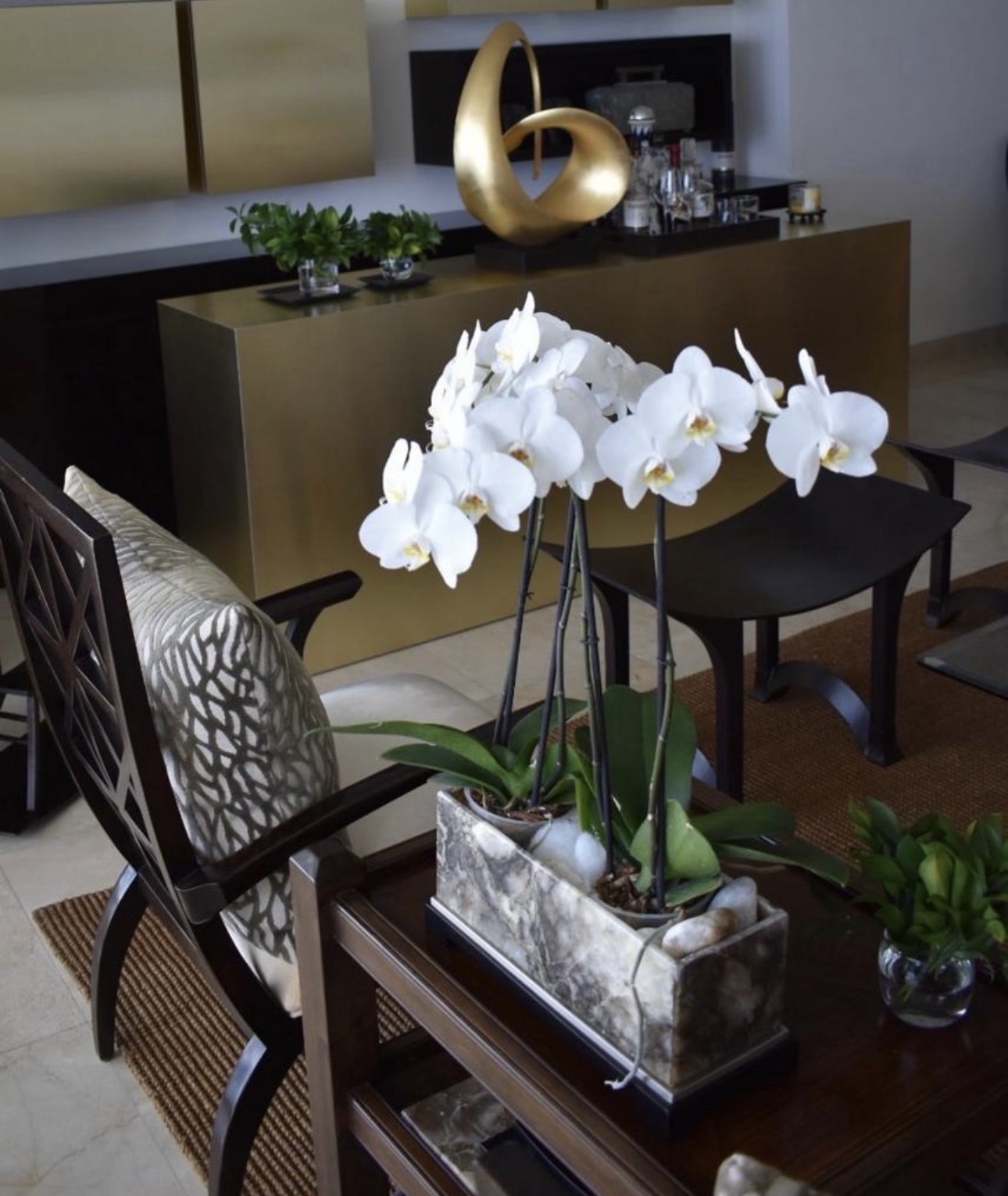 Bar con orquídeas blancas, silla con cojín texturizado y arte en tonos bronce y crema