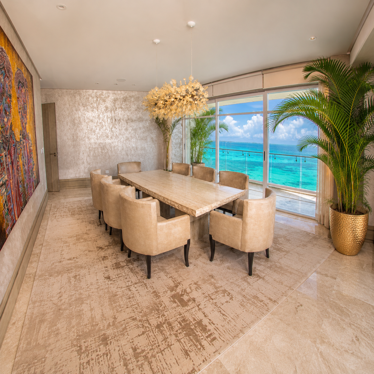Comedor frente al mar con mesa de mármol, sillones beige y candil dorado